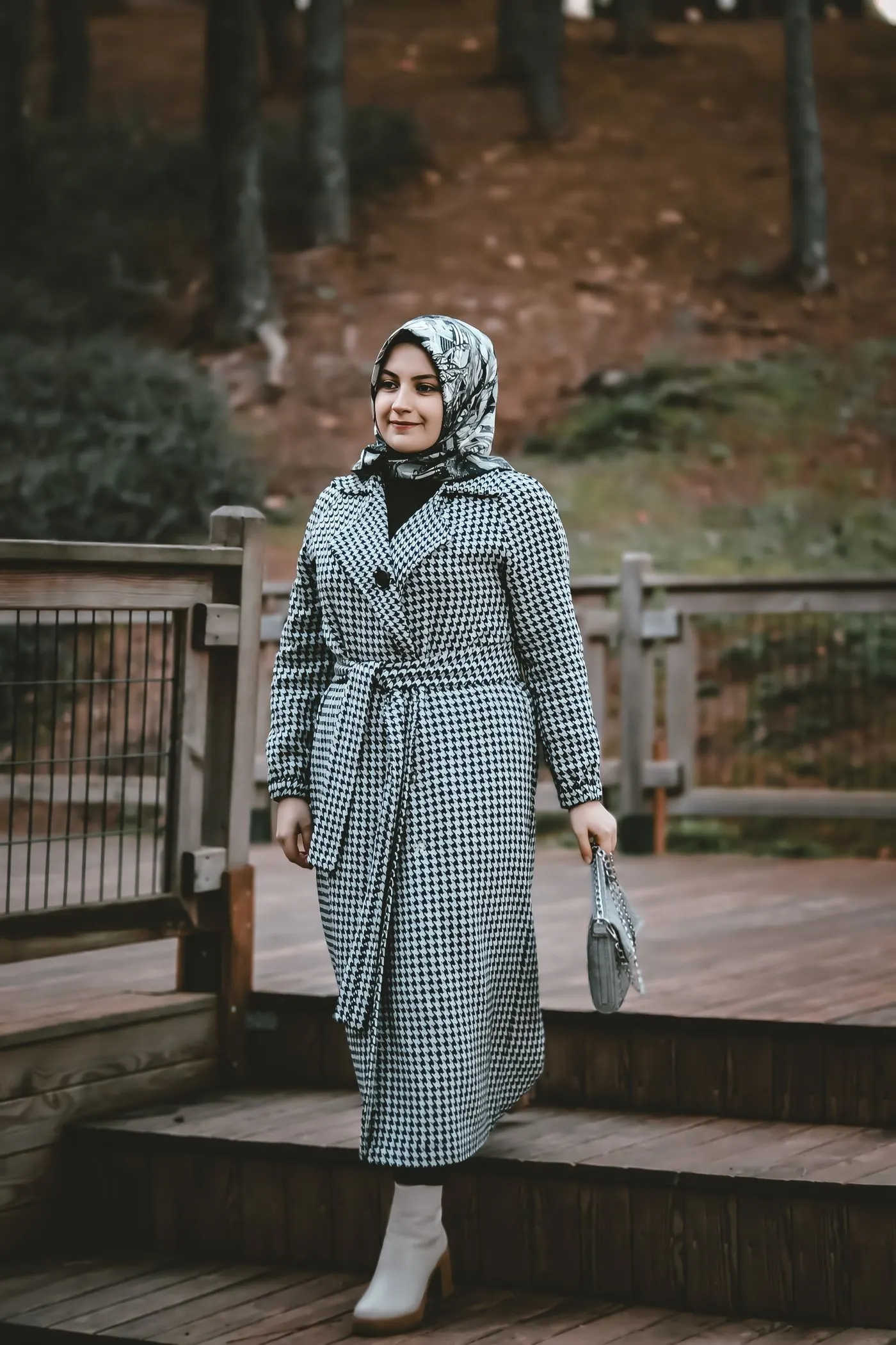 A woman in a long coat and headscarf walking along a wooden path