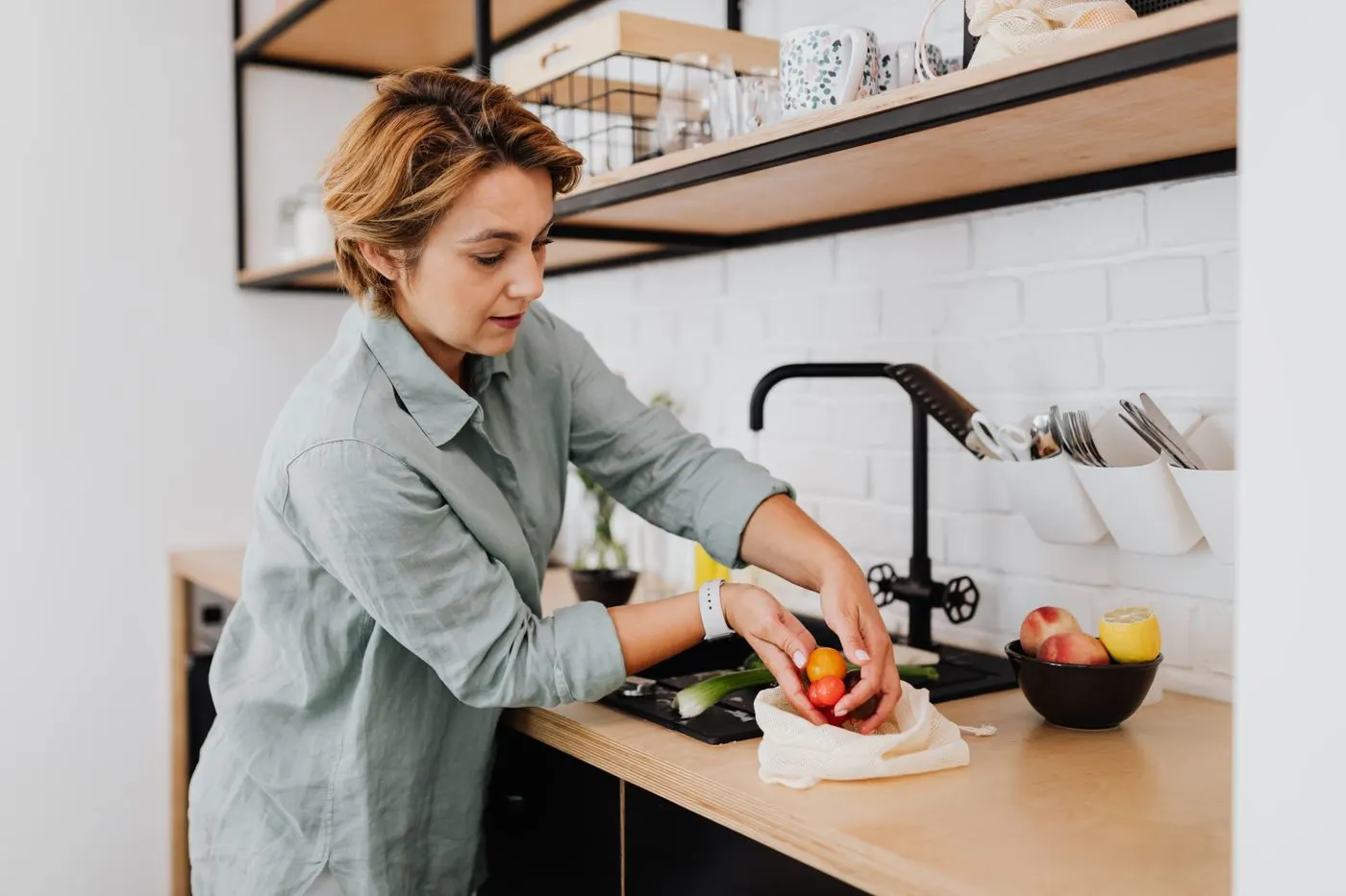A woman rinsing fresh fruit at a kitchen sink
