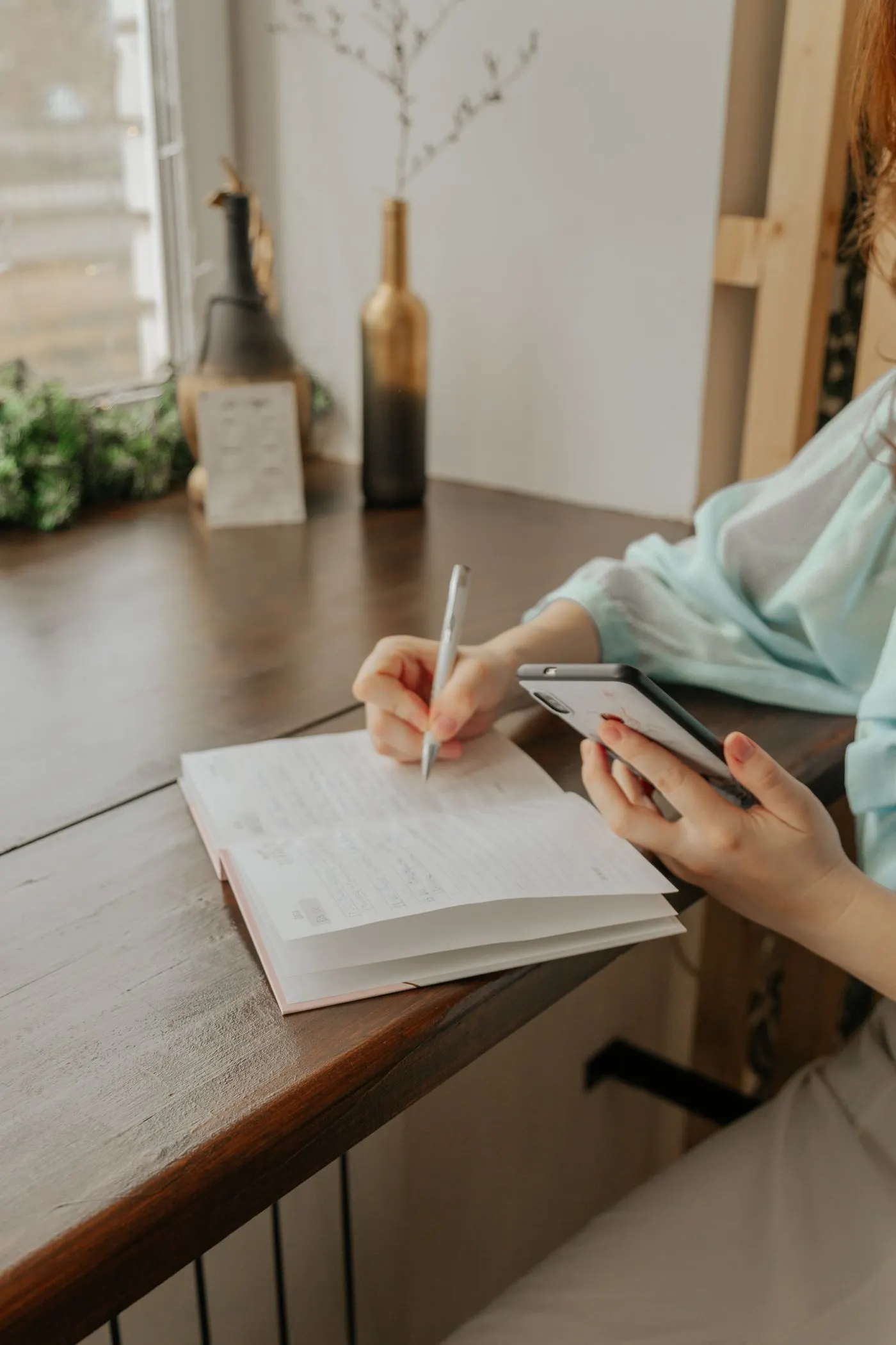 Hands writing in a notebook beside a phone